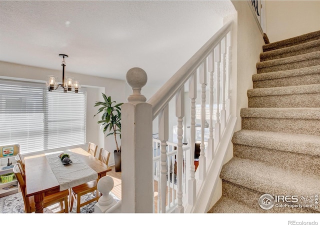 stairway with a textured ceiling and an inviting chandelier