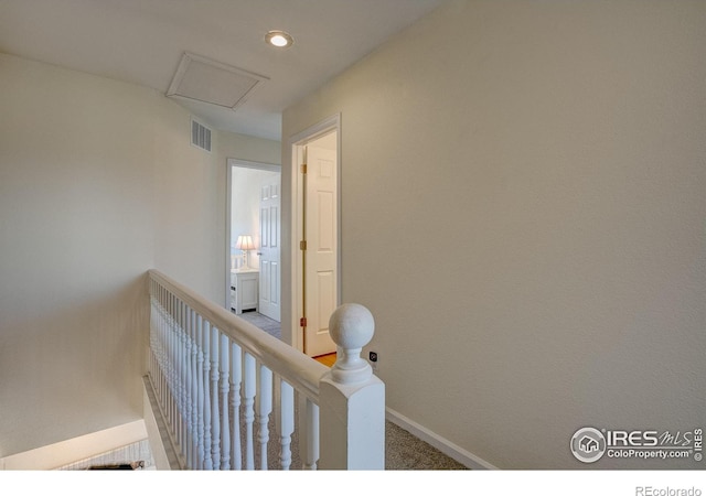 corridor featuring carpet floors, an upstairs landing, baseboards, visible vents, and attic access