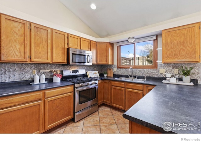 kitchen featuring vaulted ceiling, appliances with stainless steel finishes, dark countertops, and a sink