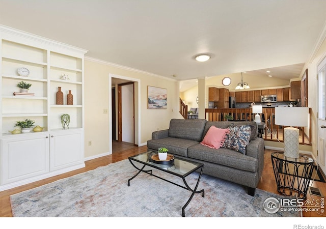 living area with crown molding, ornate columns, wood finished floors, baseboards, and stairs