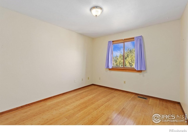 spare room with baseboards, visible vents, and wood finished floors