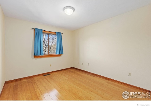 empty room with baseboards, visible vents, and wood finished floors