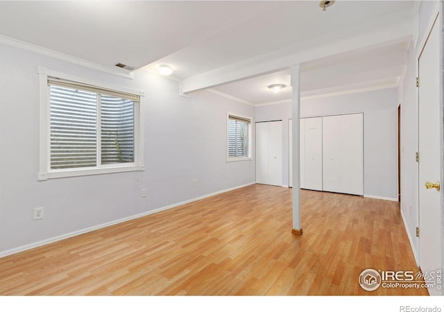 unfurnished bedroom with visible vents, baseboards, wood finished floors, crown molding, and multiple closets