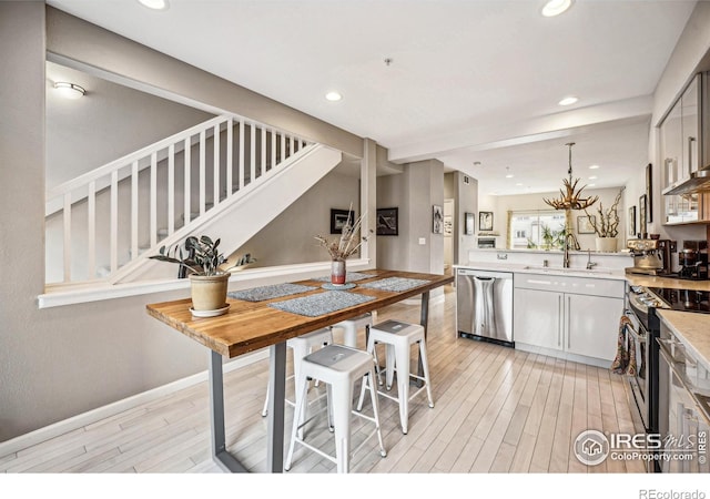 kitchen featuring stainless steel appliances, light countertops, a sink, light wood-type flooring, and a peninsula