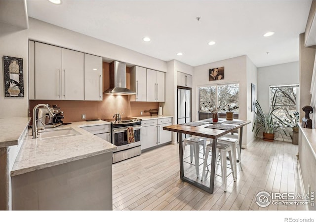 kitchen featuring light wood-style floors, stainless steel appliances, wall chimney range hood, a sink, and recessed lighting