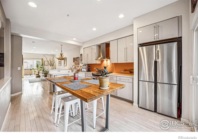 kitchen featuring recessed lighting, light wood-style floors, light countertops, appliances with stainless steel finishes, and wall chimney range hood