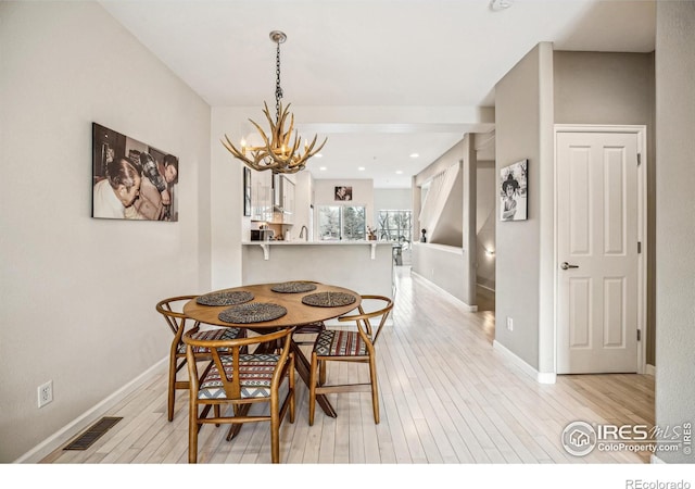 dining area with light wood-type flooring, an inviting chandelier, baseboards, and visible vents