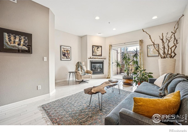 living area with wood finished floors, recessed lighting, a glass covered fireplace, and baseboards