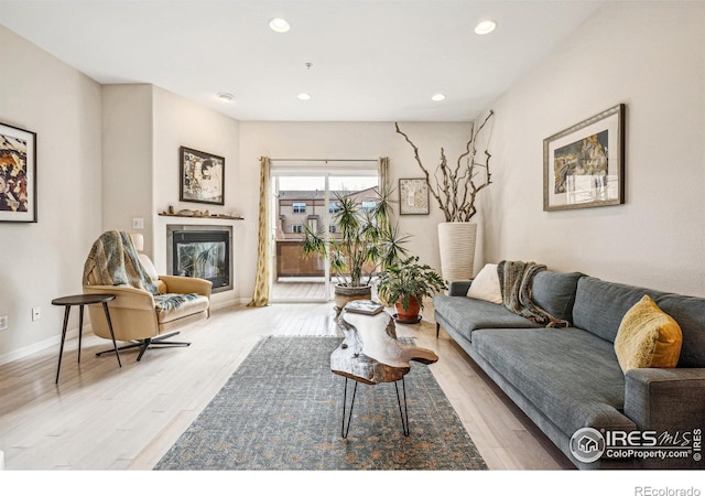 living area featuring baseboards, wood finished floors, a glass covered fireplace, and recessed lighting