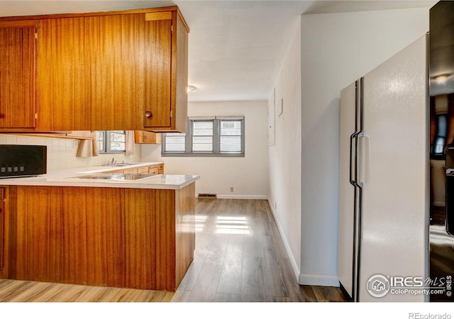 kitchen featuring brown cabinetry, freestanding refrigerator, light countertops, and a peninsula