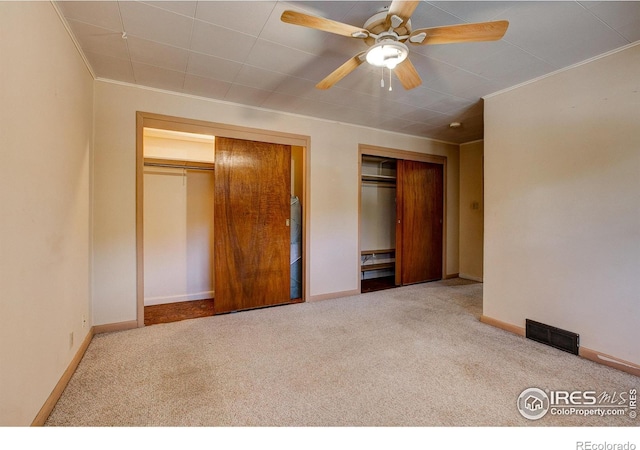 unfurnished bedroom featuring baseboards, carpet, visible vents, and two closets