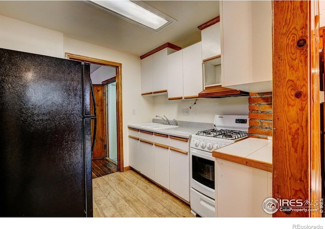 kitchen with freestanding refrigerator, white cabinets, a sink, and gas range gas stove