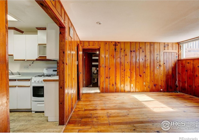 kitchen featuring wood walls, light wood-type flooring, white cabinets, and white range with gas cooktop