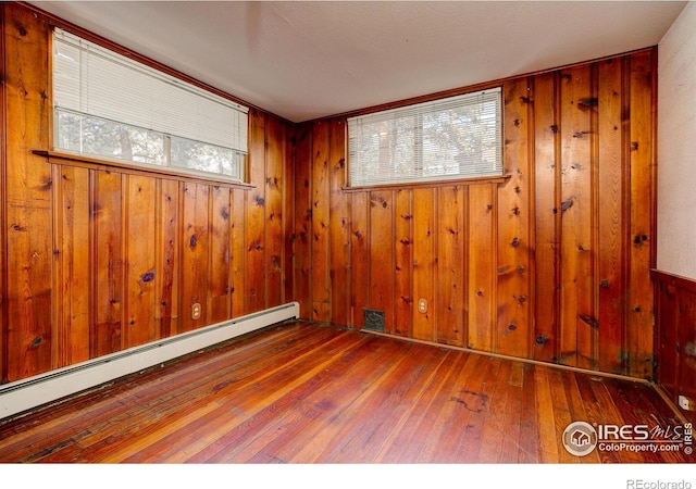 spare room with a baseboard radiator, wooden walls, and hardwood / wood-style floors