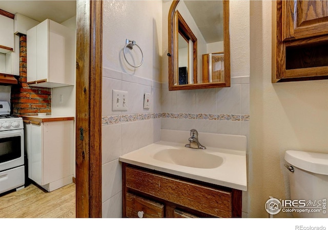 bathroom with decorative backsplash, toilet, wood finished floors, vanity, and tile walls