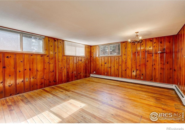 empty room with wood walls, a baseboard radiator, and hardwood / wood-style floors