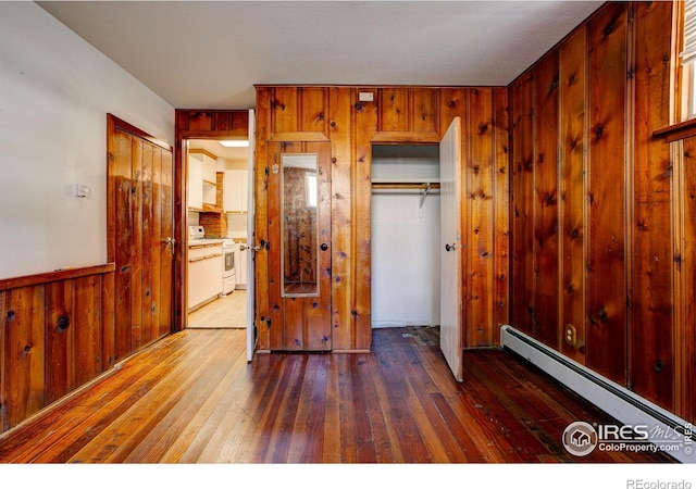 bedroom with wood walls, a baseboard radiator, hardwood / wood-style floors, and a wainscoted wall