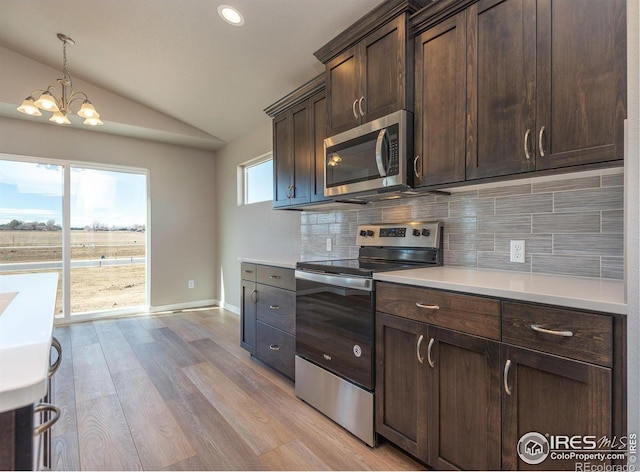 kitchen with tasteful backsplash, lofted ceiling, appliances with stainless steel finishes, light countertops, and light wood-style floors