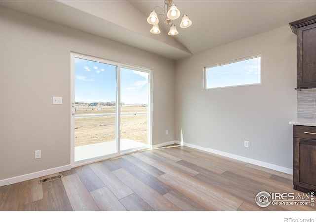 unfurnished dining area featuring light wood-style flooring, visible vents, a chandelier, and baseboards