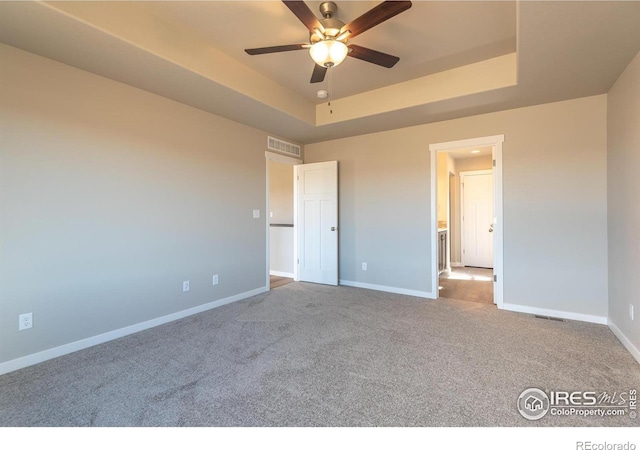 unfurnished bedroom featuring a tray ceiling, carpet flooring, visible vents, and baseboards