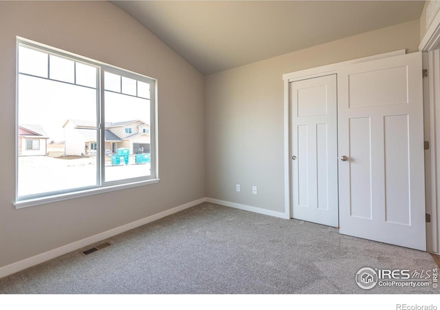 unfurnished bedroom with baseboards, visible vents, vaulted ceiling, carpet flooring, and a closet