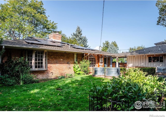 rear view of property featuring roof mounted solar panels, brick siding, a lawn, and a chimney