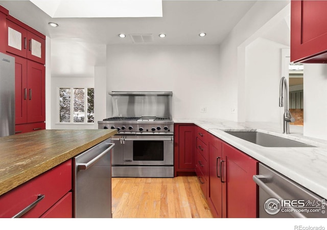 kitchen featuring stainless steel appliances, visible vents, red cabinetry, a sink, and light wood-type flooring