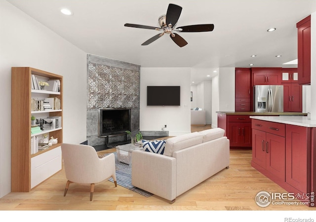 living room with a ceiling fan, recessed lighting, light wood finished floors, and a tile fireplace