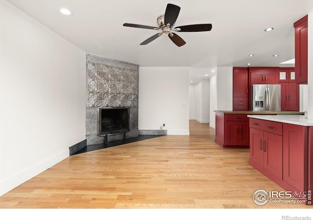 kitchen with light wood finished floors, stainless steel fridge, a tile fireplace, open floor plan, and dark brown cabinets