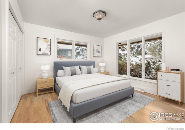 bedroom featuring baseboards, light wood-style flooring, visible vents, and a closet