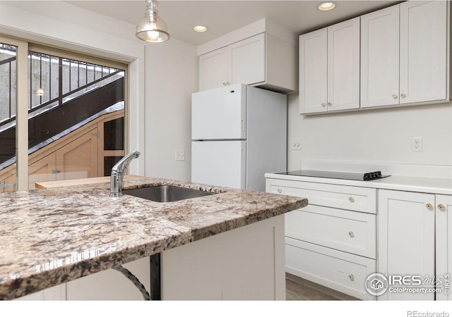 kitchen featuring light stone counters, recessed lighting, freestanding refrigerator, white cabinets, and a sink