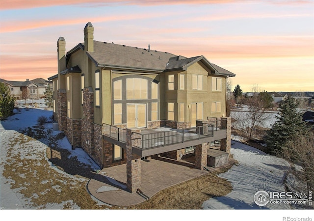 back of house at dusk with a patio, a chimney, and stucco siding