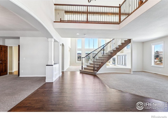 carpeted entryway with stairs, a high ceiling, baseboards, and ornate columns