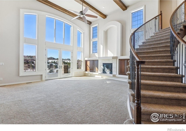 unfurnished living room featuring a ceiling fan, a towering ceiling, beamed ceiling, carpet flooring, and a fireplace