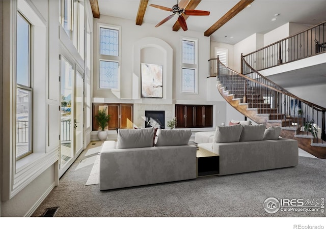 carpeted living room with stairs, beamed ceiling, a glass covered fireplace, and a towering ceiling