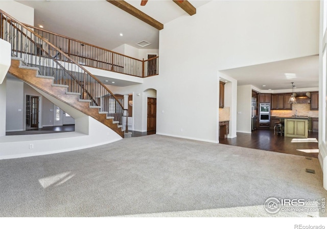 unfurnished living room featuring arched walkways, stairway, beam ceiling, dark colored carpet, and a sink