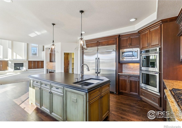 kitchen with dark wood-style floors, dark countertops, a glass covered fireplace, a sink, and built in appliances