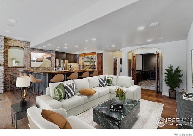 living area featuring arched walkways, recessed lighting, brick wall, wood finished floors, and ornate columns