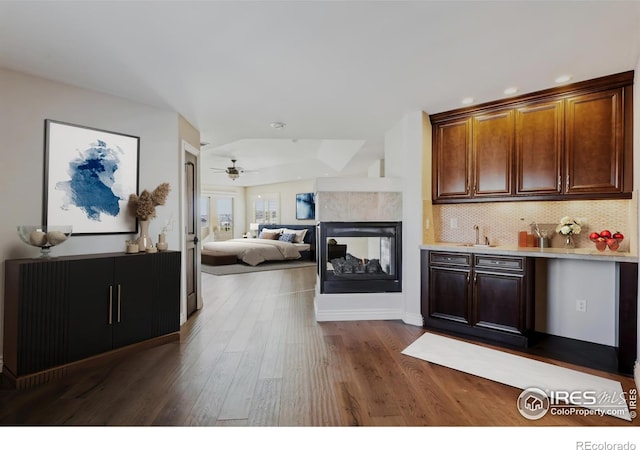 interior space featuring a multi sided fireplace, a sink, a ceiling fan, decorative backsplash, and dark wood-style floors