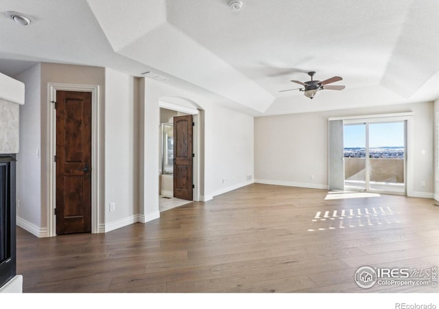 unfurnished living room featuring baseboards, a ceiling fan, a raised ceiling, and wood finished floors