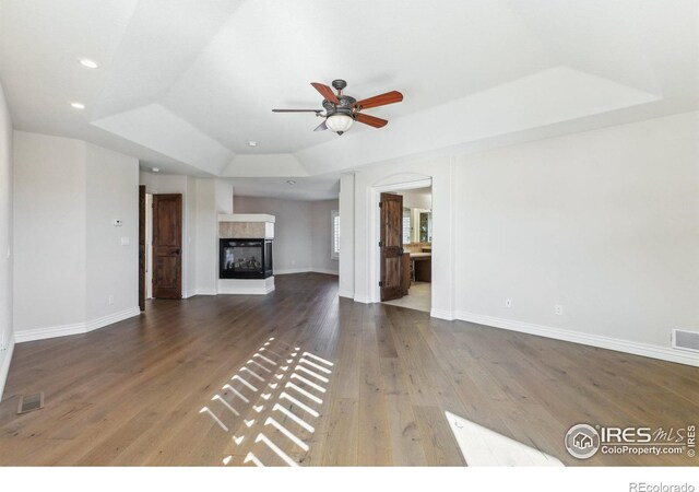 unfurnished living room with baseboards, a tray ceiling, wood finished floors, and a multi sided fireplace