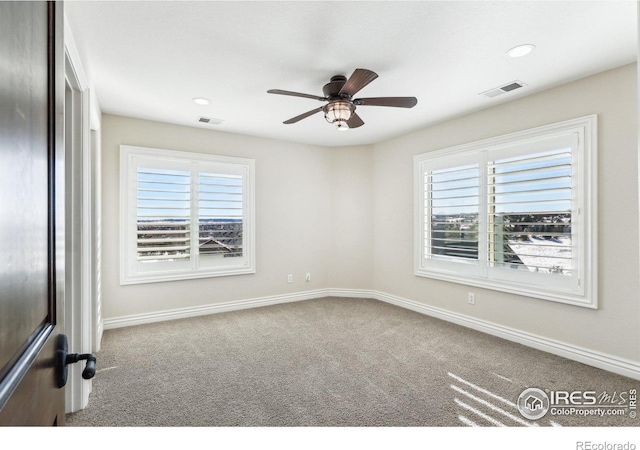 carpeted spare room featuring a ceiling fan, visible vents, and baseboards