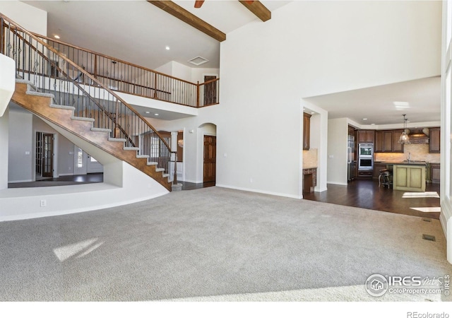 unfurnished living room with dark carpet, baseboards, a high ceiling, stairway, and arched walkways