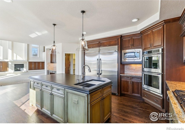 kitchen with built in appliances, a sink, dark wood-style floors, dark countertops, and a premium fireplace