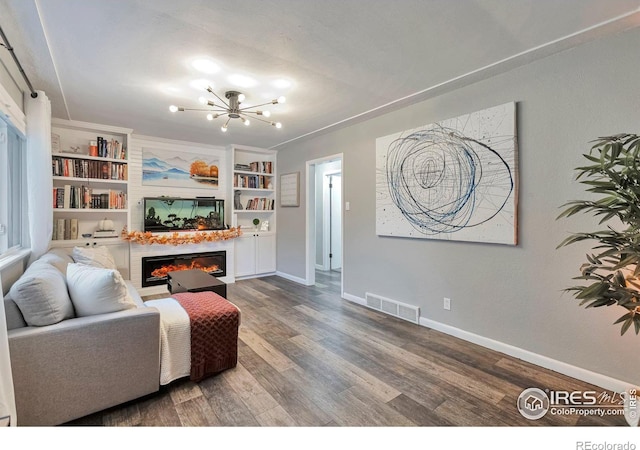 living area with wood finished floors, visible vents, baseboards, a glass covered fireplace, and an inviting chandelier