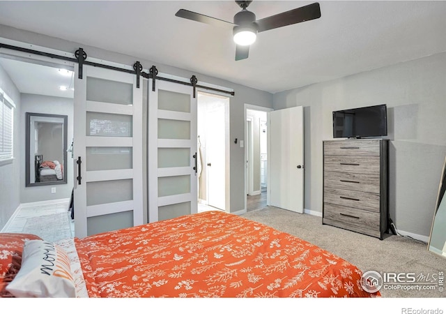 carpeted bedroom with a barn door, baseboards, and ceiling fan