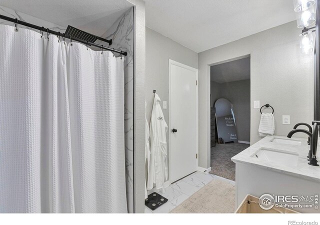 full bath featuring marble finish floor, double vanity, a sink, and a shower with curtain