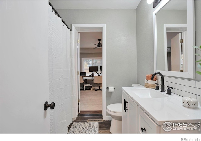 bathroom featuring a ceiling fan, toilet, wood finished floors, vanity, and backsplash