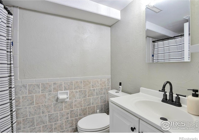 full bath with tile walls, visible vents, a textured wall, toilet, and vanity