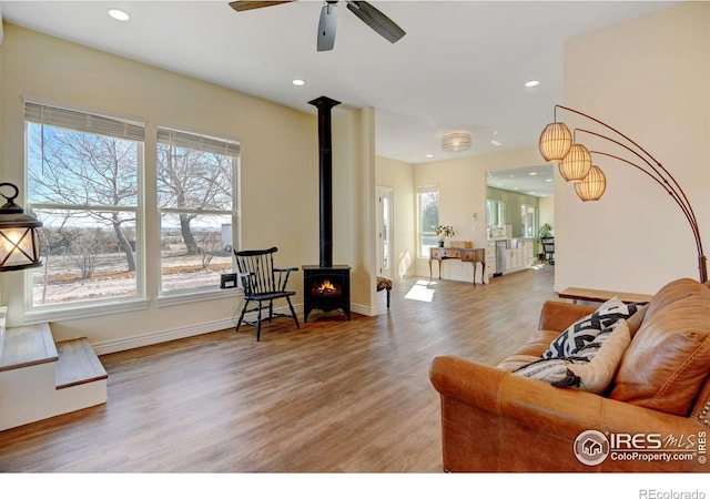 living room with baseboards, a ceiling fan, light wood-style flooring, a wood stove, and recessed lighting